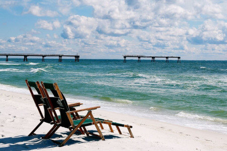 beach shot with ocean in background, camera is focusing on two beach chairs