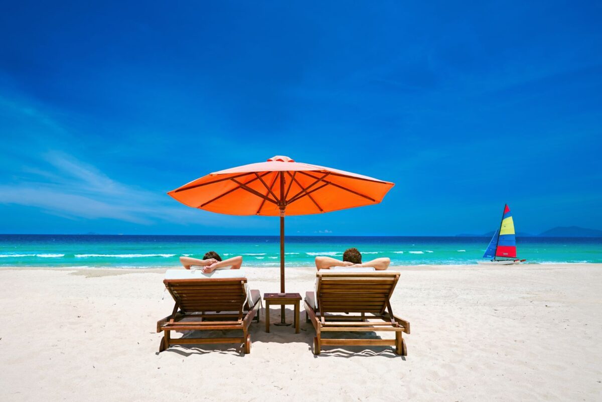 Two people relaxing on PCB beach under umbrella